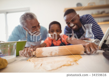 Boy preparing cookie dough with his father and grandfather in kitchen Boy preparing cookie dough with his father and grandfather in kitchen 34359616