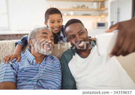 Smiling multi-generation family taking selfie from mobile phone in living room 34359657