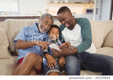 Smiling multi-generation family using mobile phone in living room Smiling multi-generation family using mobile phone in living room 34359664