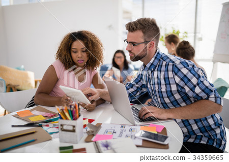 Male and female executives discussing over digital tablet in the office 34359665
