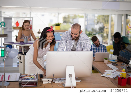Male and female executives discussing over computer at desk Male and female executives discussing over computer at desk 34359751