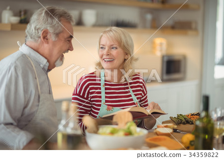 Senior couple reading recipe book while preparing meal 34359822