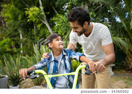 Father and son standing with bicycle while looking at each other 34360892