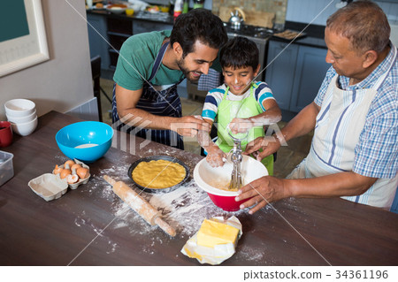 High angle view of father and grandfather looking at boy making food High angle view of father and grandfather looking at boy making food 34361196