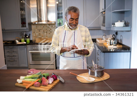 Smiling man using tablet computer while cooking food Smiling man using tablet computer while cooking food 34361321