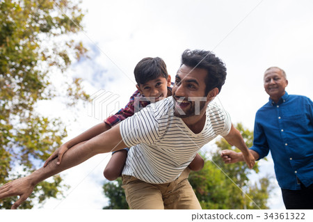 Happy grandfather looking at man giving piggy backing to son 34361322