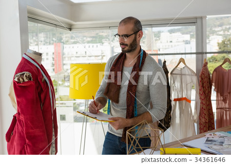 Designer writing on paper while looking at mannequin 34361646