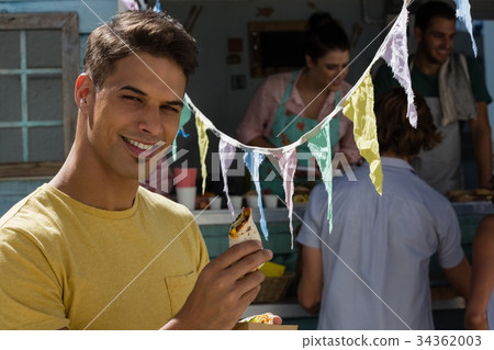 Young man eating tortilla while standing by food truck 34362003