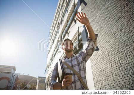 Man holding disposable cup gesturing while walking by building in city 34362205
