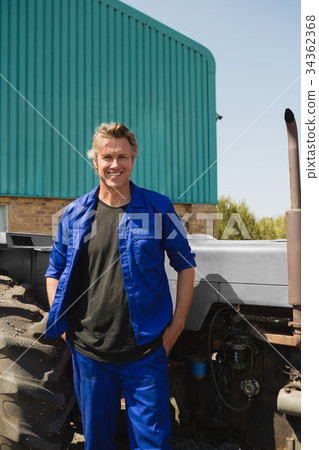 Worker standing with hands in pocket near tractor Worker standing with hands in pocket near tractor 34362368