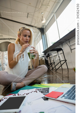 Woman having drink while working on floor at office 34362430