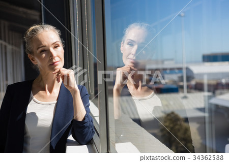 Thoughtful businesswoman looking through window at office Thoughtful businesswoman looking through window at office 34362588