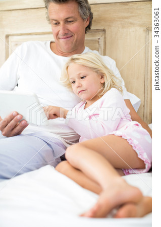 Smiling father and daughter using digital tablet on bed Smiling father and daughter using digital tablet on bed 34363061