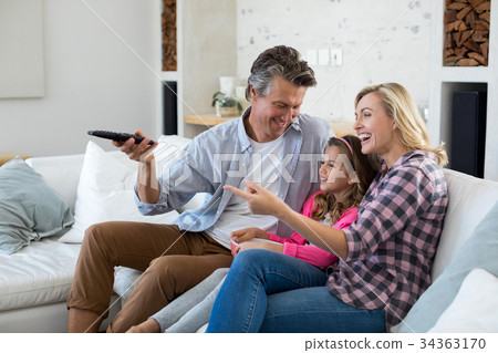 Smiling family watching television while having popcorn in living room 34363170