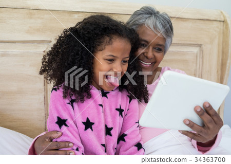 Grandmother and granddaughter using digital tablet in bed room 34363700