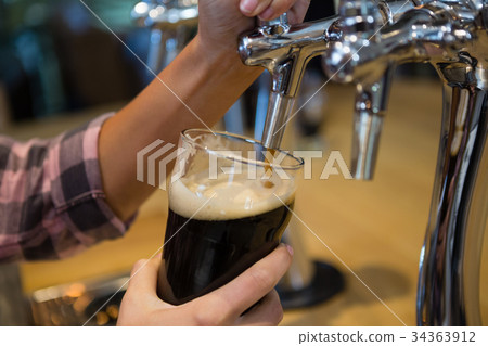 Cropped hands of barmaid pouring drink from tap in glass 34363912