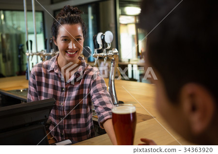Smiling barmaid serving drink to man 34363920