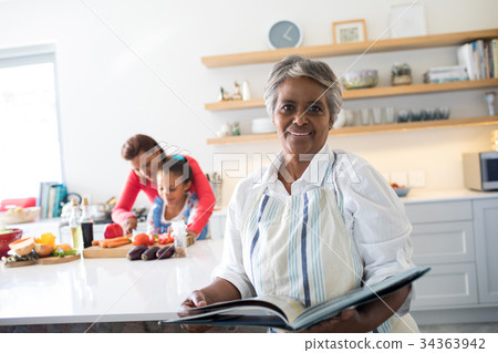 Portrait of smiling senior woman holding recipe book in kitchen 34363942