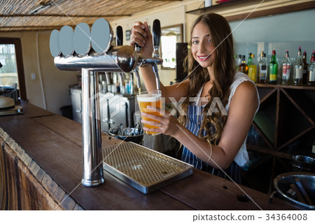 Portrait of young barmaid pouring beer from tap in glass 34364008