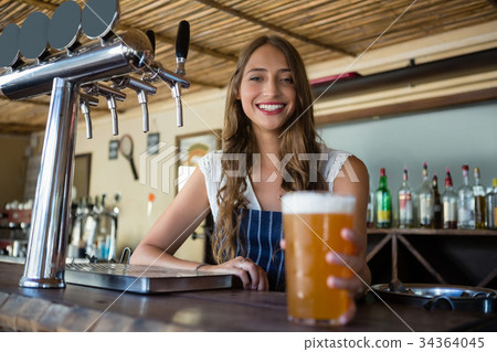 Portrait of happy barmaid holding beer glass 34364045