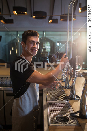 Portrait of bartender pouring beer from tap at bar 34364083
