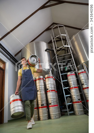 Low angle view of worker with kegs walking at warehouse 34364096