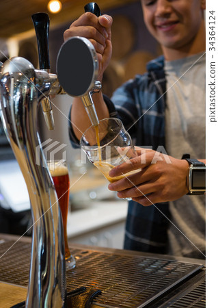 Bartender pouring drink from tap in glass at bar 34364124