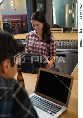 Female owner using cash register by customer at bar counter 34364202