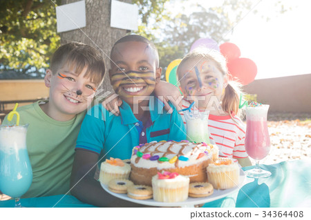 Happy children with face paint having food and drinks at park 34364408