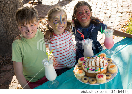 Happy friends with face paint sitting by food and drink at table 34364414