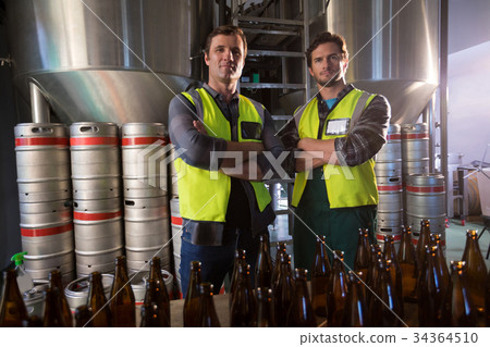 Portrait of coworkers with arms crossed standing by beer bottles Portrait of coworkers with arms crossed standing by beer bottles 34364510