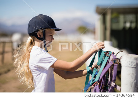 Girl picking up a horse muzzle in the ranch 34364584