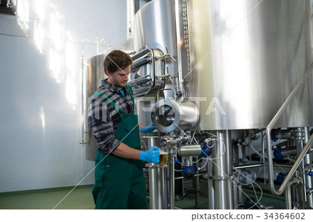 Male worker taking beer from storage tank at factory 34364602