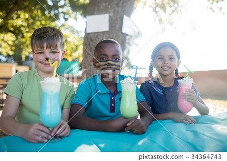 Smiling children with face paint having drinks at park 34364743