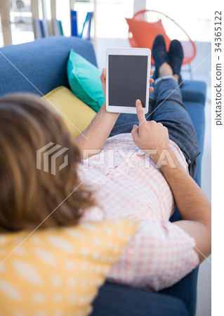 Male executive using digital tablet while relaxing on sofa Male executive using digital tablet while relaxing on sofa 34365122