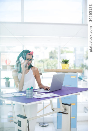 Executive talking on mobile phone while using laptop in office 34365128