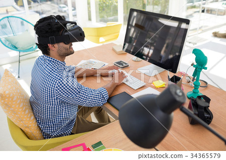 Graphic designer in virtual reality headset working on computer at desk Graphic designer in virtual reality headset working on computer at desk 34365579