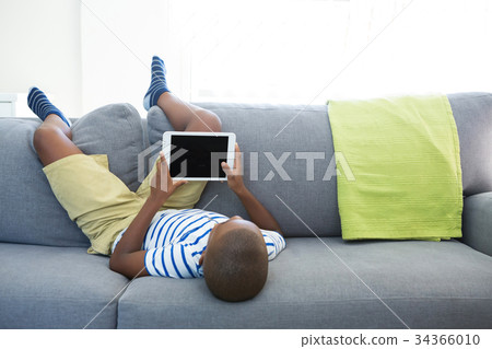 Boy lying on sofa while using digital tablet at home Boy lying on sofa while using digital tablet at home 34366010