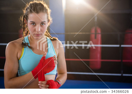 Portrait of young female athlete wrapping red bandage on hand Portrait of young female athlete wrapping red bandage on hand 34366026