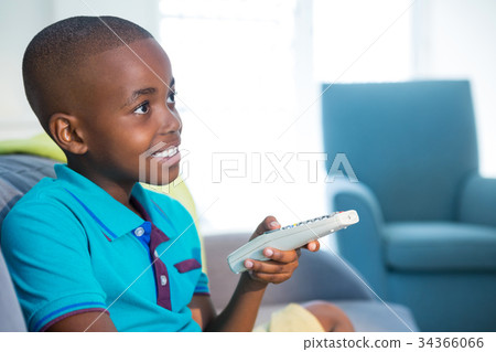 Smiling boy holding remote control on sofa at home 34366066