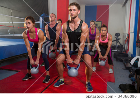 Group of young athletes lifting kettles by boxing ring 34366096