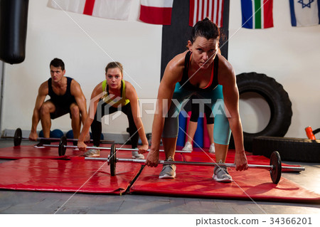 Portrait of female athlete lifting barbell with friends Portrait of female athlete lifting barbell with friends 34366201