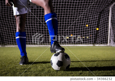 Low section of male soccer player standing with ball on field 34366232