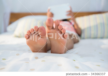 Girl lying on bed while using digital tablet 34366337
