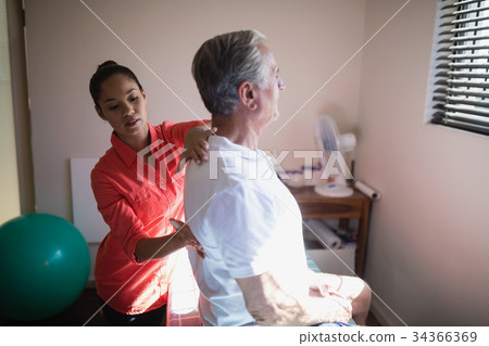 Young female therapist massaging back of senior male patient 34366369
