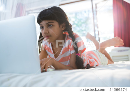 Tilt shot of girl using laptop on bed Tilt shot of girl using laptop on bed 34366374