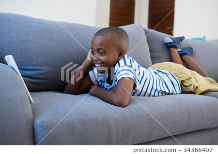 Smiling boy looking at mobile phone while lying on gray sofa 34366407