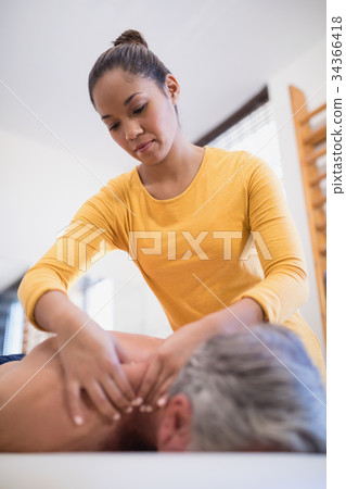 Low angle view of female therapist giving neck massage to male patient Low angle view of female therapist giving neck massage to male patient 34366418