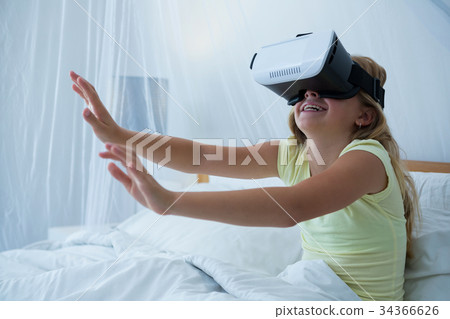 Girl using virtual reality simulator while sitting on bed 34366626