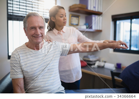Portrait of smiling senior male patient with female doctor examining hand Portrait of smiling senior male patient with female doctor examining hand 34366664